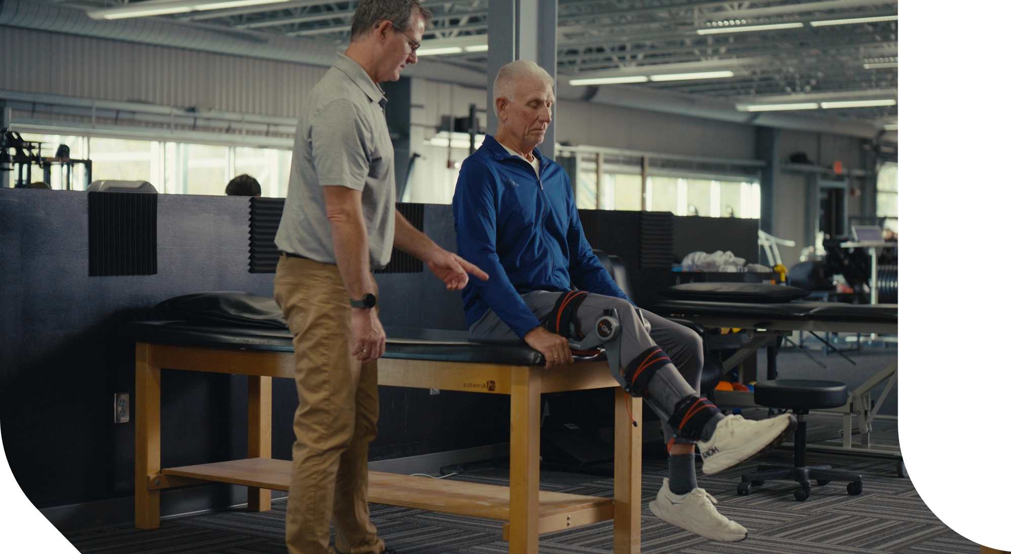 Two men in a room with one on a wooden platform and the other assisting him.
